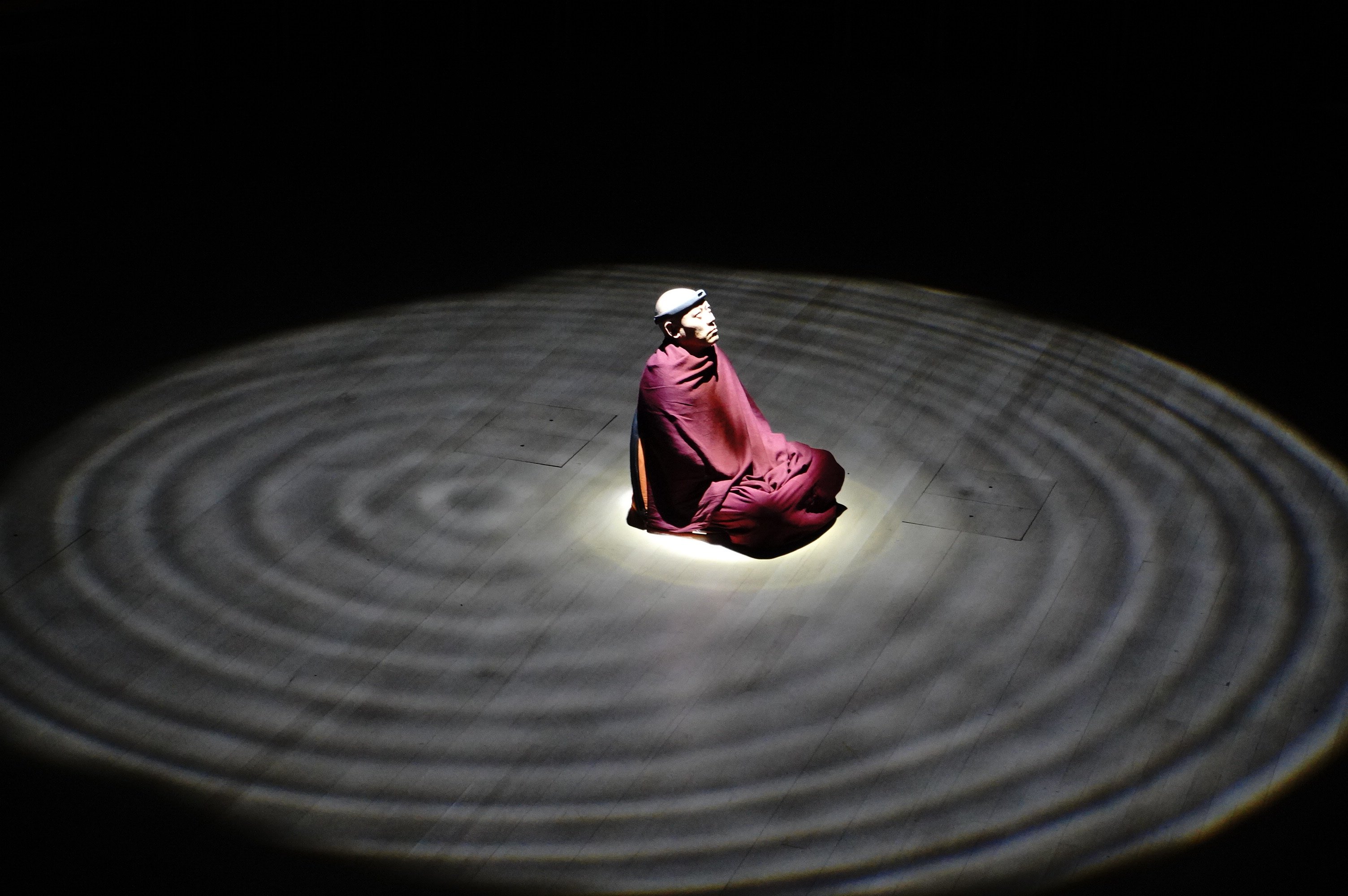Monk in meditation surrounded by projected wave patterns at MIT Music Hall